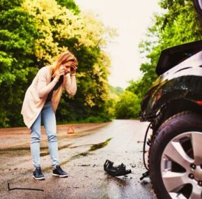 Frustrated woman standing in front of car talking on the phone after a car crash accident