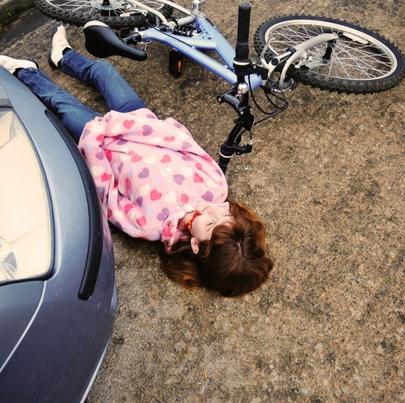 Little girl knocked off bike, lying dead by car, eyes open. She is not wearing a helmet.