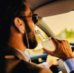 Man drinking alcohol while driving a car. Danger on the road caused by drunk drivers.