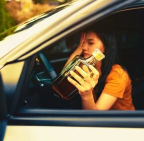 Drunk female driver holding a bottle of alcoholic drink