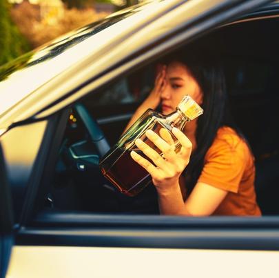 Drunk female driver holding a bottle of alcoholic drink