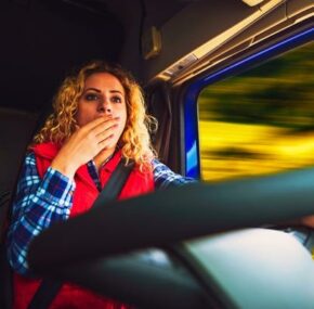 Sleep deprived lady truck driver yawning while driving