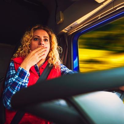 Sleep deprived lady truck driver yawning while driving