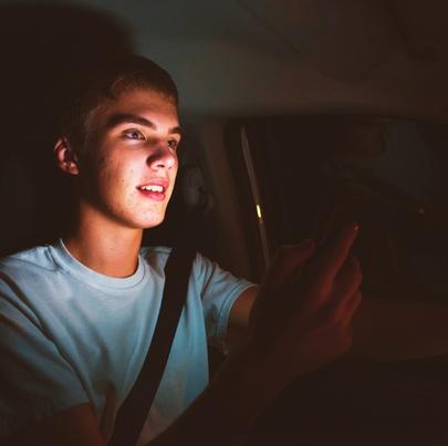 Distracted teenage driver holding his phone while driving a car