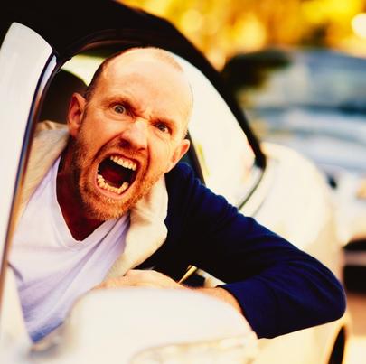 A furiously angry man driving yells through the car window in a bout of uncontrollable road rage.