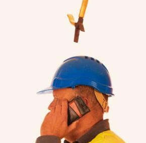 Pliers falling from a workers head, wearing a hard hat while he is talking on the phone