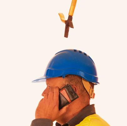 Pliers falling from a workers head, wearing a hard hat while he is talking on the phone
