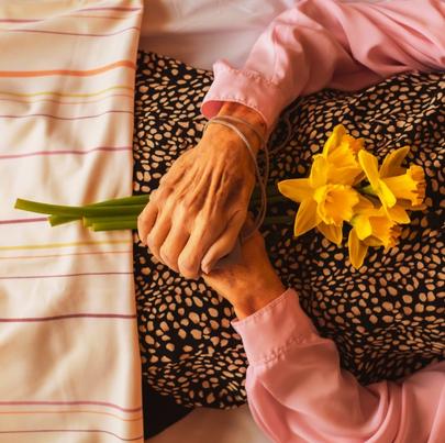 Dead elderly woman's crossed hands with flowers in her nursing home death bed