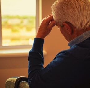 Sad and depressed male senior left alone in a room facing window of a nursing home window