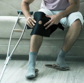 man sitting on a couch while putting on knee support with crutches on the side