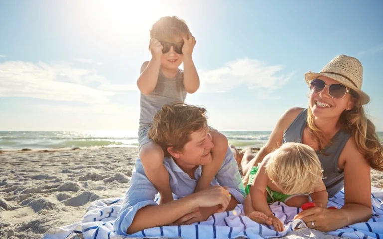 Family smiling on a beach blanket at the beach practicing beach safety.